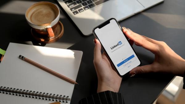 Iskalec zaposlitve za mizo gleda Linkedin aplikacijo na telefonu